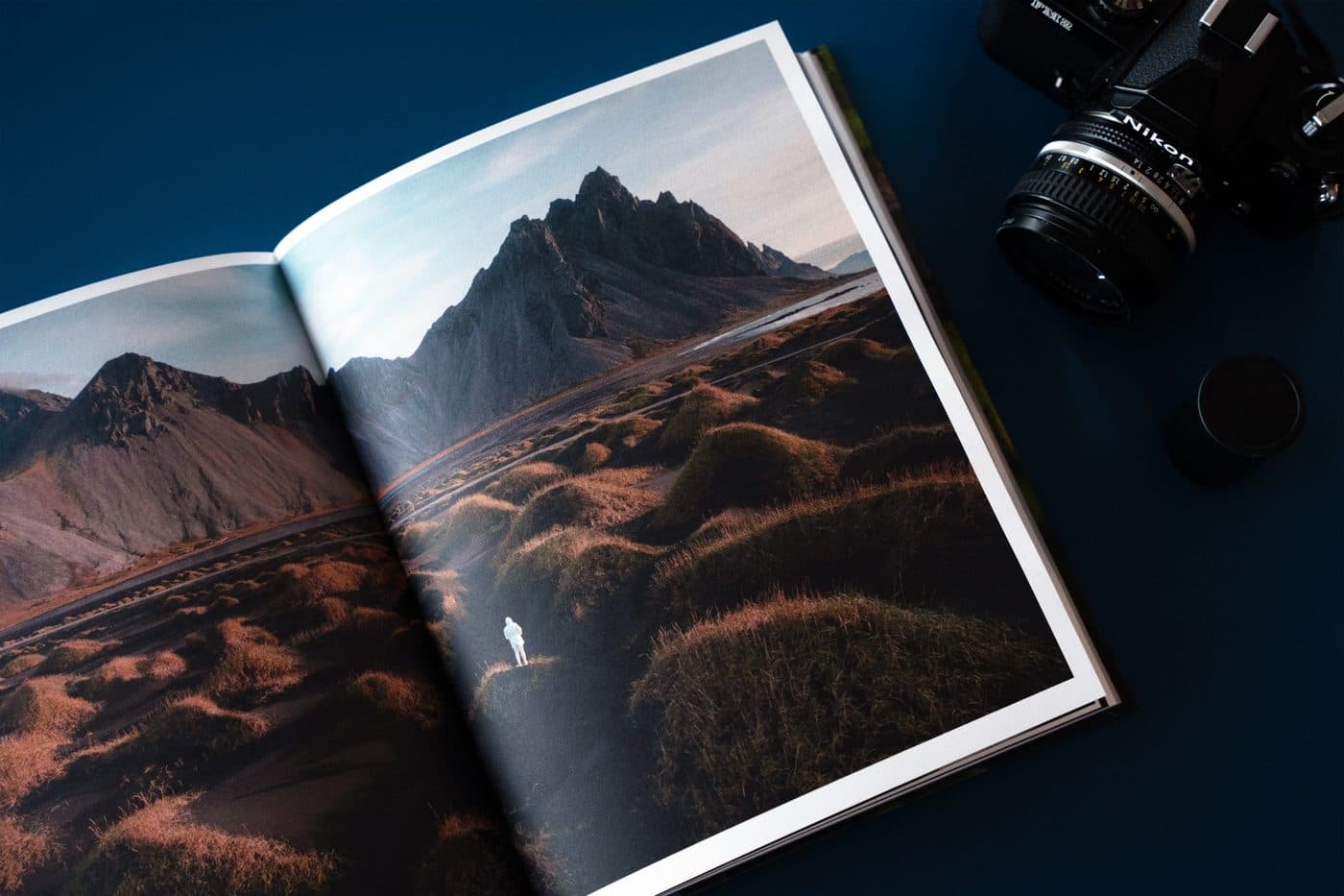 An open Blurb travel book showing an Iceland mountain spread, next to a film camera
